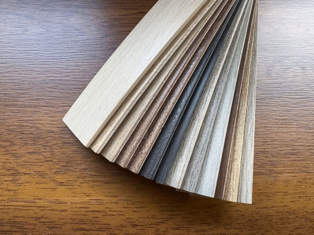 A fan-shaped arrangement of various wood veneer samples showcasing different colors and textures. The samples range from light to dark shades, displayed on a wooden surface.