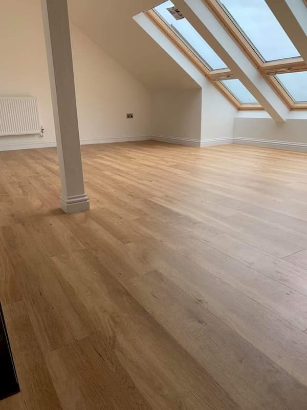 A spacious attic room with light wood flooring, sloping ceilings, and large skylight windows allowing natural light in. A radiator is mounted on the left wall and the room is empty, highlighting its open and airy feel.